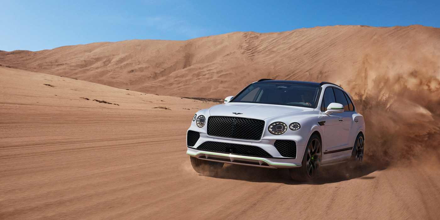 Bentley Leeds Bentley Bentayga Speed SUV front three quarter in Snow Quarts Pearlescent by Mulliner white paint driving dynamically through the desert