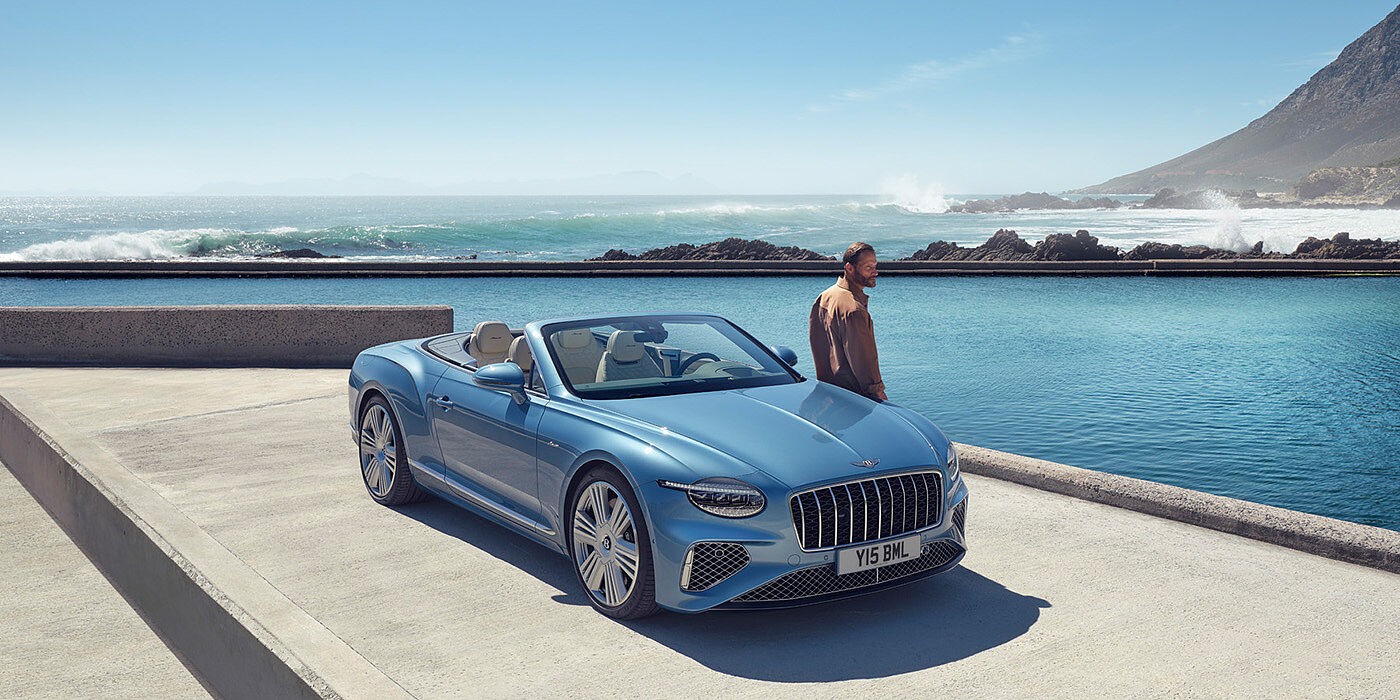 Bentley Leeds New Bentley Continental GTC Azure convertible front view in Light Windsor blue paint with 22 inch ten spoke wheels parked by the sea in the sunshine