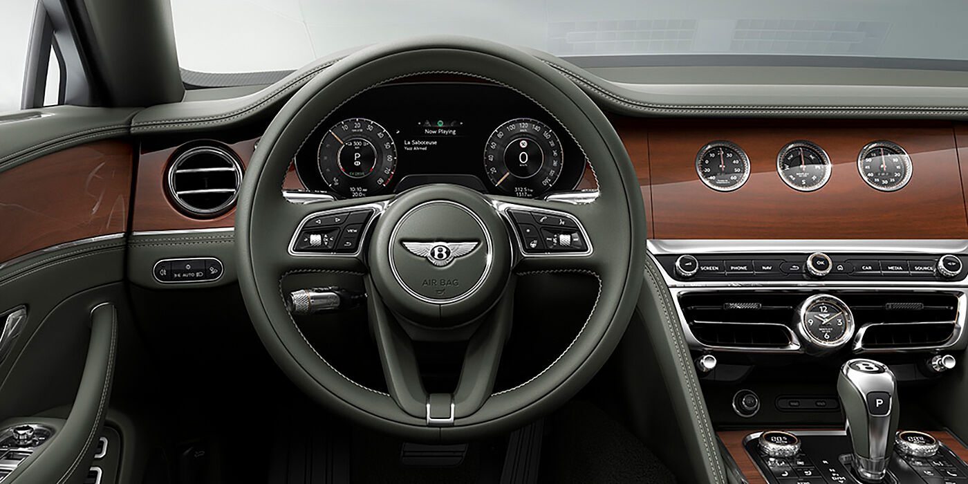 Bentley Leeds New Bentley Flying Spur sedan front cabin in Cumbrian Green hide and Crown Cut walnut veneer showing steering wheel and Rotating Display with three clocks on face