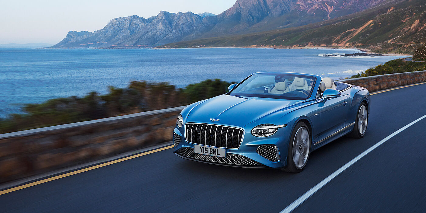 Bentley Leeds New Bentley Continental GTC Azure convertible in Light Windsor blue paint with 22 inch Azure wheels and chrome grill, driving dynamically by the sea