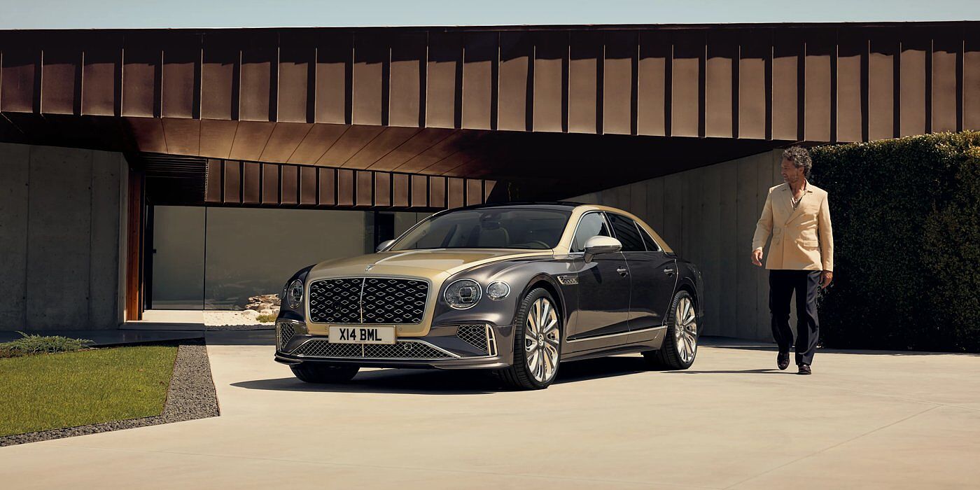 Bentley Leeds Bentley New Flying Spur Mulliner V8 hybrid sedan front three quarters in Rose Gold over Magnetic paint, parked near modern home