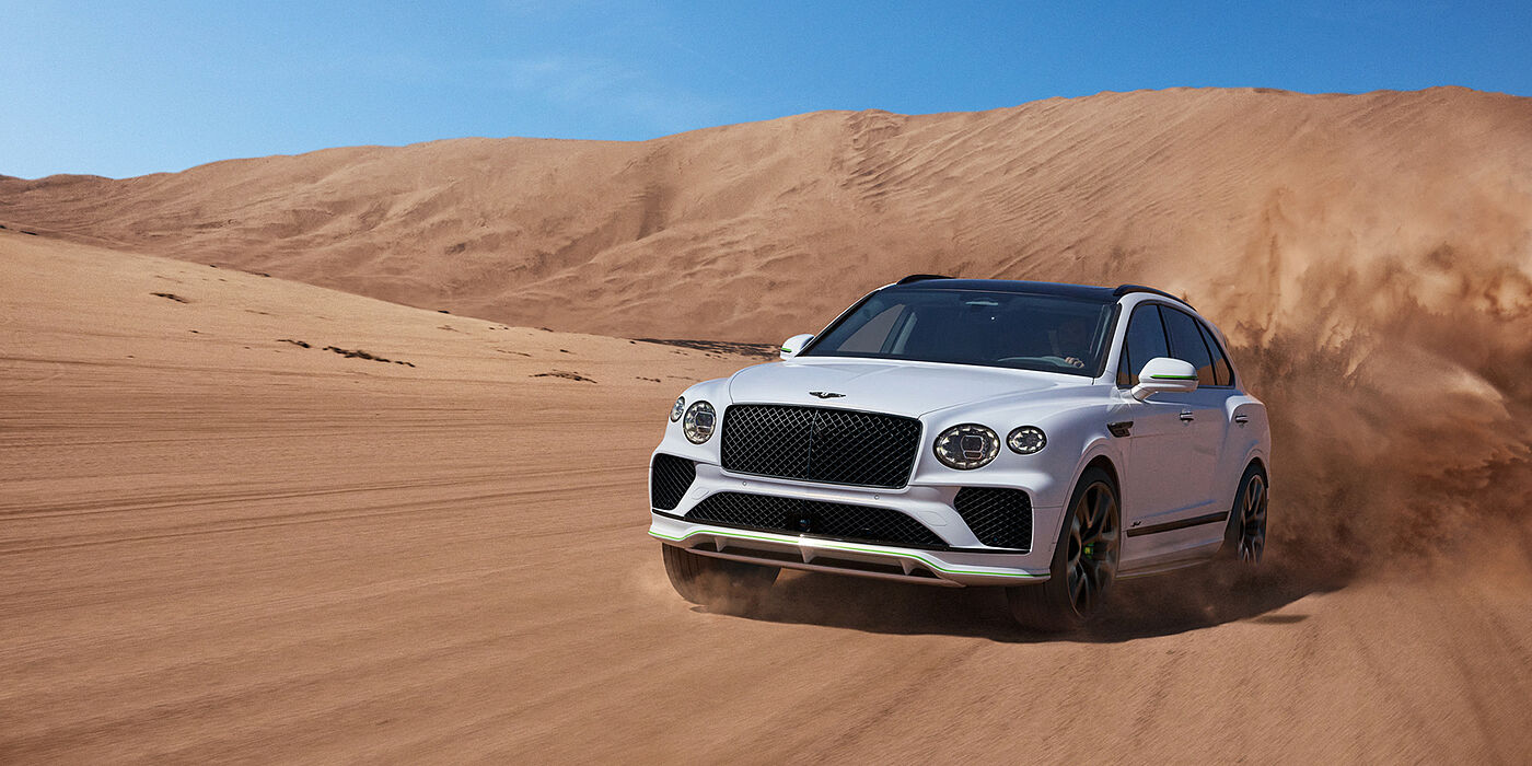Bentley Leeds Bentley Bentayga Speed SUV front three quarter in Snow Quarts Pearlescent by Mulliner white paint driving dynamically through the desert