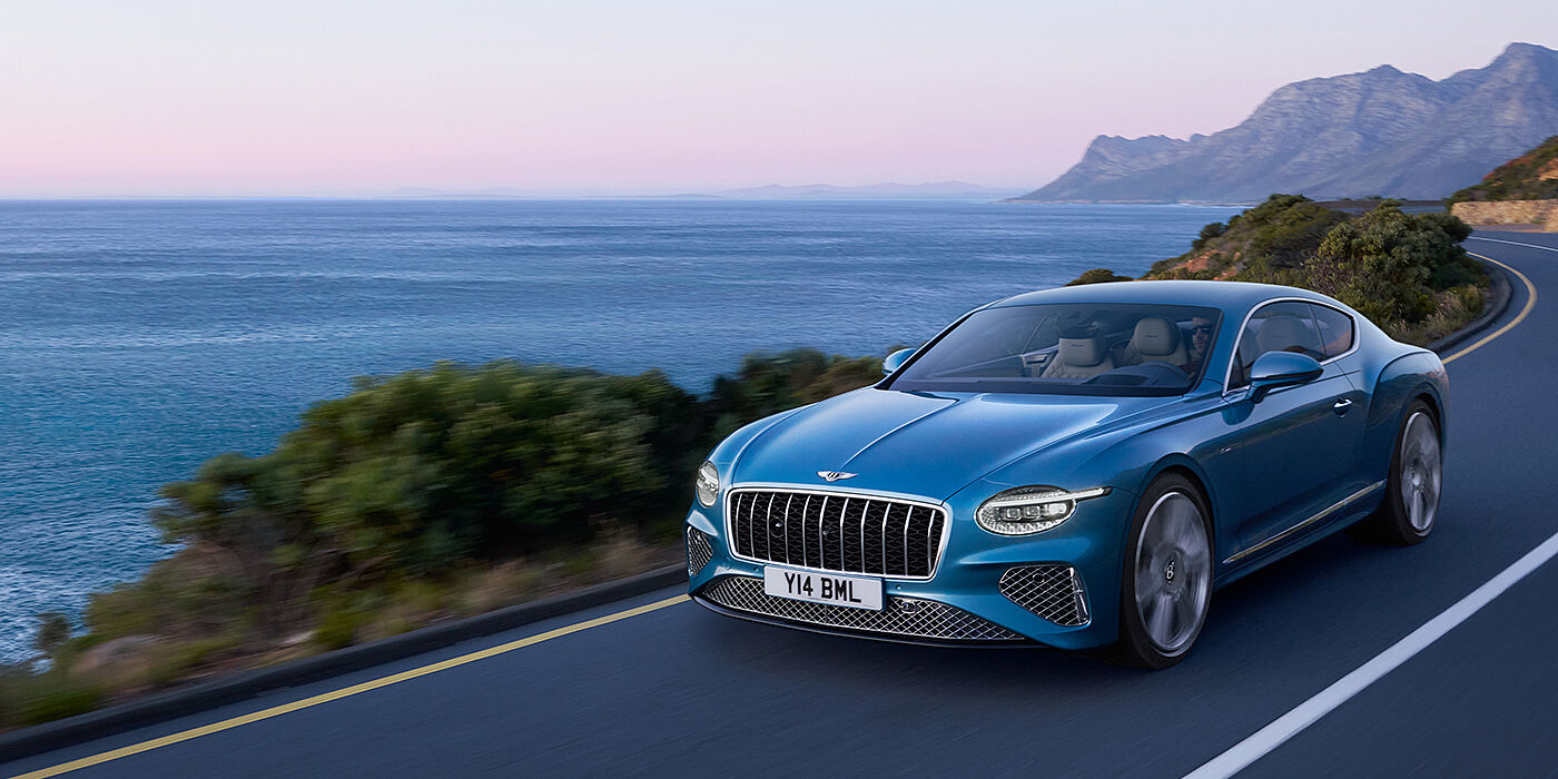 Bentley Leeds New Bentley Continental GT Azure coupe in Light Windsor blue paint with 22 inch Azure wheels and chrome grill, driving dynamically by the sea