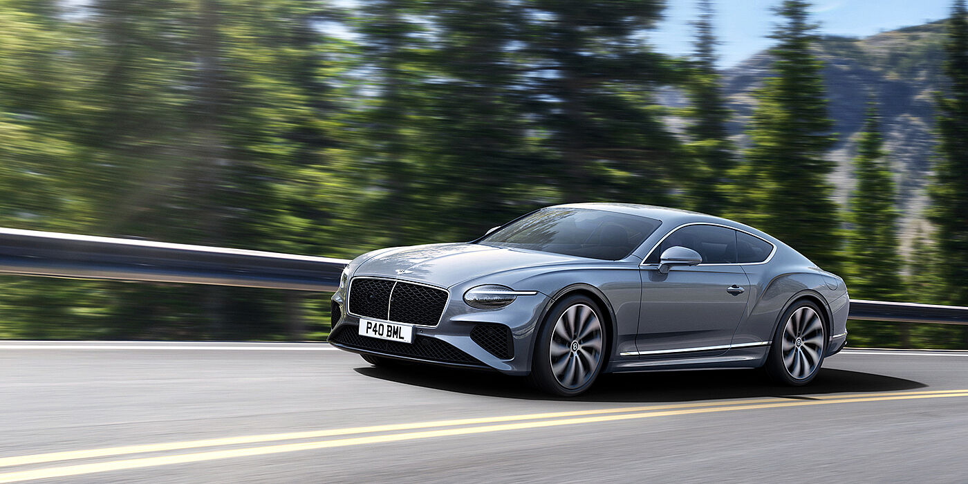 Bentley Leeds New Bentley Continental GT coupe in Silverlake paint and 22 inch ten-spoke wheels, driving dynamically on a tree-lined road in the sunshine