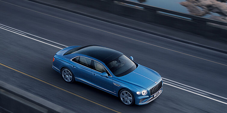 Bentley Leeds New Bentley Flying Spur Azure sedan in Light windsor blue paint by Mulliner, with 22 inch Azure wheels seen from overhead driving dynamically on a country road
