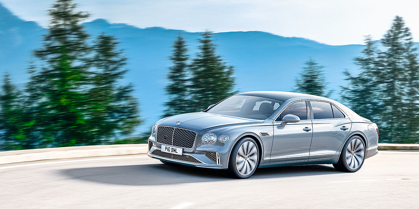 Bentley Leeds New Bentley Flying Spur sedan side view in Silverlake paint with ten spoke wheels and chrome matrix grille driving dynamically on a mountain road