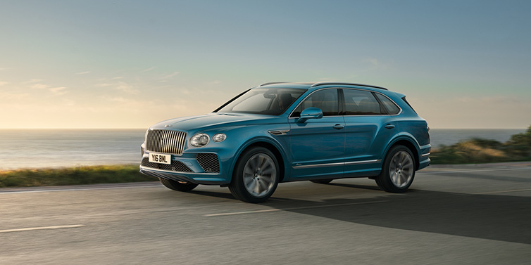 Bentley Leeds Bentley Bentayga Azure SUV in Topaz blue paint driving dynamically by the ocean with 22 inch 10 spoke directional wheels