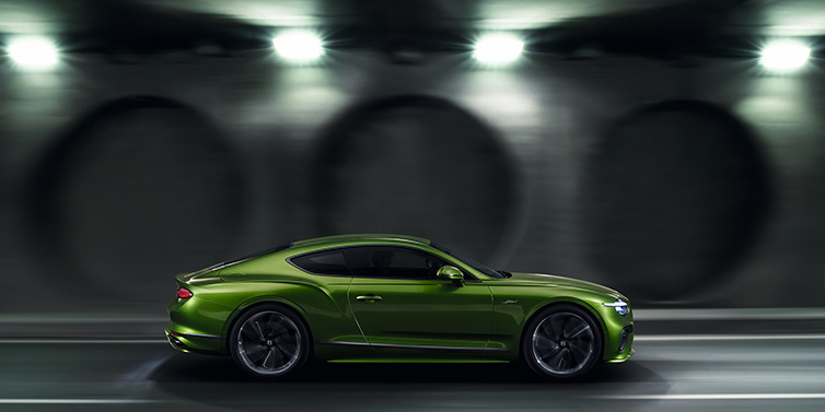 Bentley Leeds Bentley Continental GT Speed coupe profile in Tourmaline Green driving dynamically past a concrete wall at night