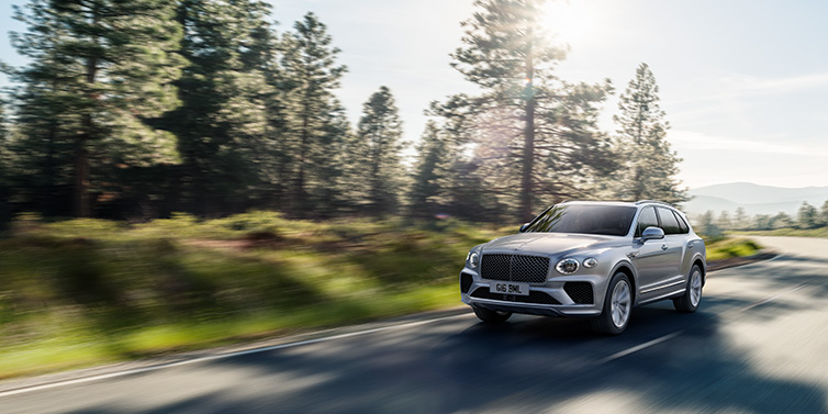 Bentley Leeds Bentley Bentayga SUV front three quarter in Moonbeam silver paint driving dynamically along a tree-lined road