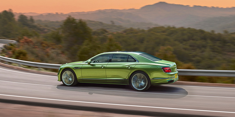 Bentley Leeds Bentley Flying Spur Speed sedan side profile in Tourmaline Green paint driving dynamically on a mountain road at sunset