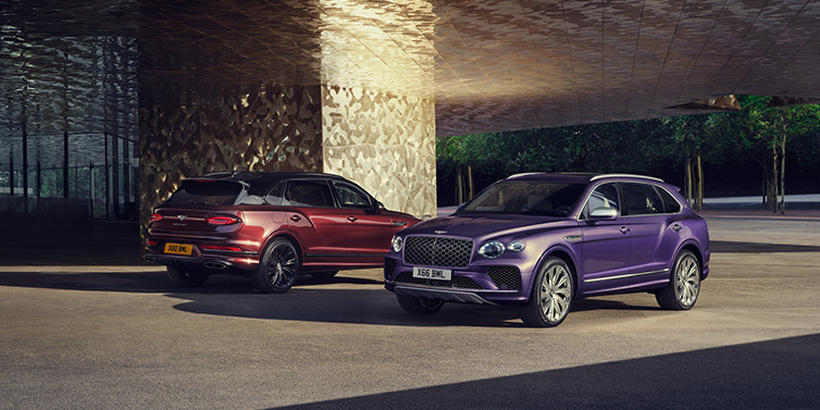 Bentley Leeds A duo of Bentley Bentayga Extended Wheelbase Mulliner SUVs parked in a city environment, with Tanzanite Purple and Cricket Ball red exterior paint