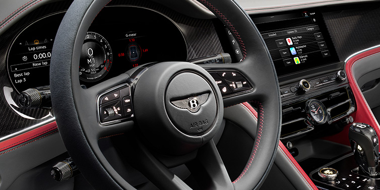 Bentley Leeds Bentley Flying Spur Speed sedan front interior detail showing steering wheel and driver screens surrounded with Hotspur red and Gravity Grey hides